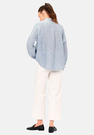 Camisa de botones a rayas en azul y blanco, de corte relajado. Combinada con pantalones anchos blancos y mocasines negros, vista desde la espalda.