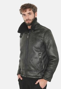 Giacca in pelle nera con finitura testurizzata, chiusura con zip frontale e colletto foderato in pelliccia. Presenta tasche laterali con zip e dettagli a contrasto.