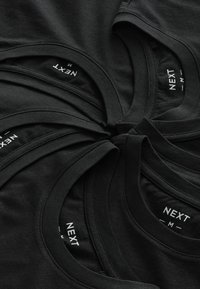 Camisetas de algodón negras apiladas, con cuellos redondeados y etiquetas que dicen "NEXT" y "M". Textura suave y diseño uniforme.