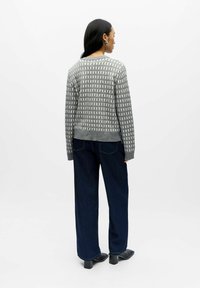 Szary sweter zapinany na guziki z wzorem, z prążkowanym dołem, w połączeniu z ciemnymi spodniami typu wide-leg i czarnymi skórzanymi botkami na obcasie. Gładka tekstura i swobodny krój.