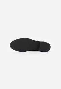 Suola di scarpa nera con superficie in gomma testurizzata, design a punta arrotondata e tacco leggero. Finitura liscia senza motivi o accenti visibili.