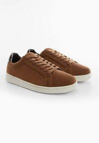 Sneakers in suede marrone con un accento in pelle nera liscia sul tallone, dotati di una suola in gomma bianca e di un design tradizionale con allacciatura.