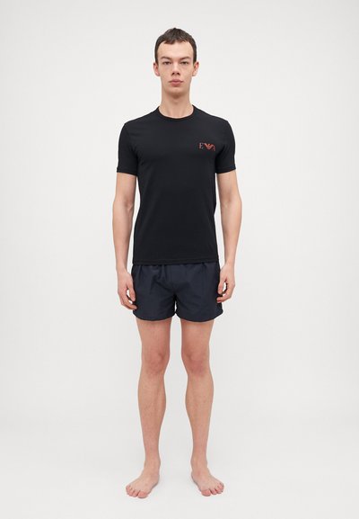 T-shirt noir à manches courtes avec un petit logo rouge sur la poitrine, accompagné de shorts bleu marine foncé. En coton, design simple et coupe ajustée.