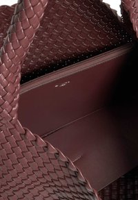 Woven burgundy leather tote bag featuring a textured exterior, smooth interior, and a zippered compartment for storage.