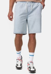 Pantalones cortos de mezclilla azul claro con cintura elástica y cordón, que cuentan con bolsillos laterales y un dobladillo recto. Llevados con zapatillas negras y blancas.
