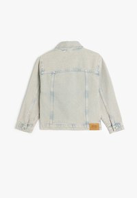 Giacca in denim azzurro chiaro con maniche lunghe, cuciture frontali e una etichetta in pelle con logo sull'orlo. Presenta un colletto classico e polsini con bottoni.
