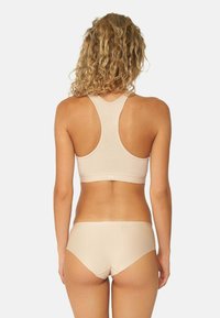 Soutien-gorge de sport beige clair avec un design dos nageur et une bande large. Culotte assortie beige clair avec une texture lisse et une coupe mi-haute.