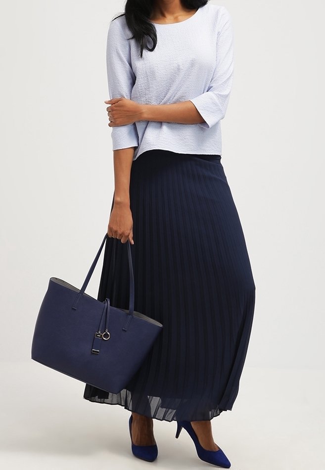 Lichtblauwe textuur top, marineblauwe plooien maxi rok, blauwe hakken en een marineblauwe leren handtas met eenvoudige hardware en twee handvatten.