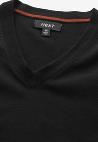 Pull noir à col en V avec une étiquette de taille M de la marque NEXT et une bande orange à l'intérieur du col.