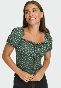 Grøn floral bluse med pufærmer, der har et smocked design, firkantet halsudskæring og et bånd, der kan ties foran. Blødt, tekstureret stof.