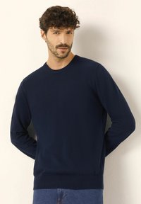 Granatowy sweter z okrągłym dekoltem, wykonany z miękkiej dzianiny, z długimi rękawami i ściągaczem na dole. Casualowy krój odpowiedni na różne okazje.