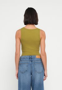 Λαδί ριμπ μπλουζάκι χωρίς μανίκια με στρογγυλή λαιμόκοψη, συνδυασμένο με τζιν παντελόνι ψηλόμεσο σε μπλε χρώμα, με επιφάνεια στο πίσω μέρος και δύο πίσω τσέπες.