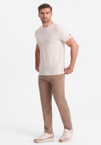 Hellbeige T-Shirt mit kurzen Ärmeln und kleinen, mehrfarbigen Punkten, kombiniert mit maßgeschneiderten braunen Hosen und hellen Sportschuhen.