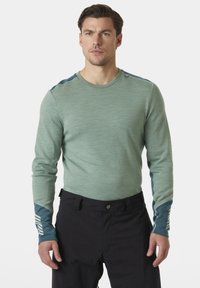 Dlouhý rukáv košile ve světle zelené barvě, se strukturovanou látkou, kulatým výstřihem a kontrastními tmavě modrými rukávy s bílými pruhy.