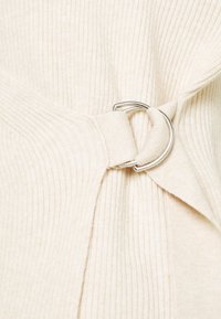 Tissu côtelé crème avec un détail en anneau métallique argenté cintrant une section froncée du matériau.