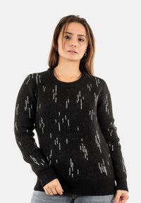 Suéter negro con patrón blanco, hecho de lana suave. Presenta un escote redondo y puños y dobladillo acanalados. Corte relajado.