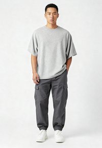 Siv majhen T-shirt z dolgimi rokavi v velikosti oversize, v kombinaciji s temnosivimi cargo hlačami z elastičnimi manšeti in več žepi, dopolnjen z belimi supergami.