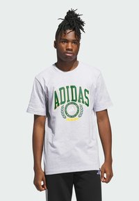 Pilkas medvilnės marškinėliai su žaliais ir geltonais „ADIDAS“ logo ir laurų grafika ant priekinės dalies. Trumpomis rankovėmis ir apvalia iškirpte.