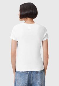 T-shirt bianco in cotone con maniche corte, scollo rotondo e un piccolo logo sul retro. Il tessuto appare liscio e leggero.