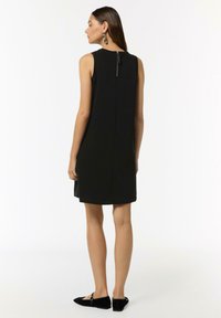 Czarna sukienka bez rękawów o wysokim dekolcie i prostym kroju, z zamkiem błyskawicznym z tyłu. W połączeniu z czarnymi płaskimi butami.