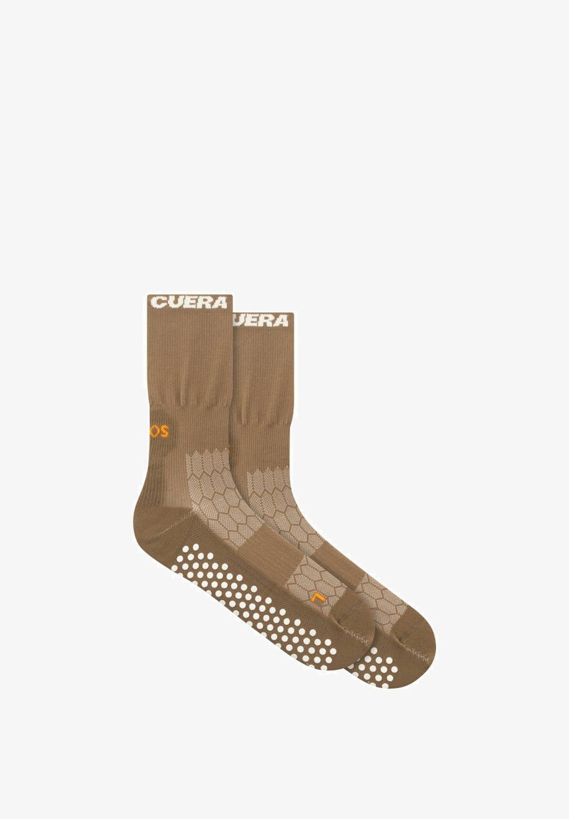 Paire de chaussettes crew marron avec motif hexagonal et points antidérapants blancs sur les semelles, avec texte blanc et orange près des bordures et des côtés.