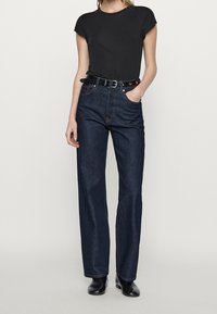 T-shirt noir à manches courtes associé à un jean en denim bleu foncé à taille haute. Tissu texturé avec une coupe droite, comportant une ceinture.