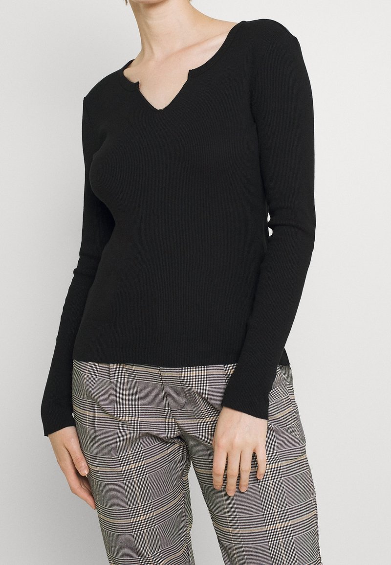 Schwarzes, gerip pt long-sleeve V-Ausschnitt-Oberteil mit strukturierter Oberfläche, kombiniert mit karierten Hosen, die ein helles und dunkles Karomuster aufweisen.