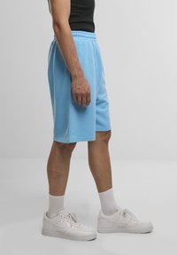 Light blue athletic shorts made of cotton blend, featuring an elastic waistband, knee-length cut, and side seam pockets. Pair with white sneakers.