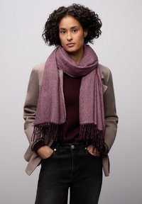 Purple herringbone-patterned scarf with fringing, draped around the neck, paired with a dark sweater and a light gray jacket.