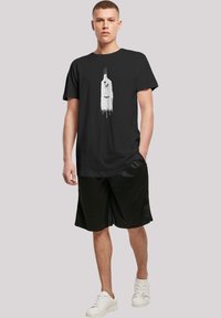 Svart t-skjorte med et hvitt grafisk design, korte ermer og relaxed fit, kombinert med svarte shorts og hvite sneakers.
