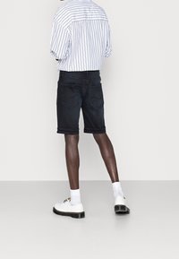 Svarta denimshorts med rak passform, utrustade med bakfickor och fransad fåll, tillsammans med en randig skjorta med knappar och vita skor.