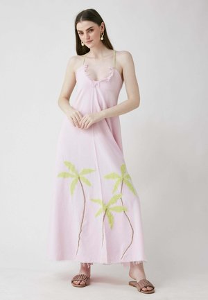 Rosa Maxikleid mit grün gestickten Palmen, gerafftem Ausschnitt und dünnen Trägern. Getragen mit braunen, strukturierten Rutschsandalen.