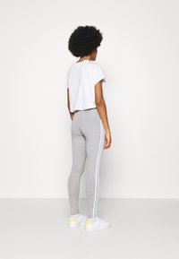 Grå leggings med vita sidostripes, ihop med en vit kortärmad skjorta och vita sneakers med gula accent. Enfärgad bakgrund.