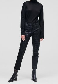 Svart polotröja matched med svarta, mönstrade skinnybyxor. Strukturerad tyg med subtil lyster. Svarta klackstövlar fulländar outfiten.