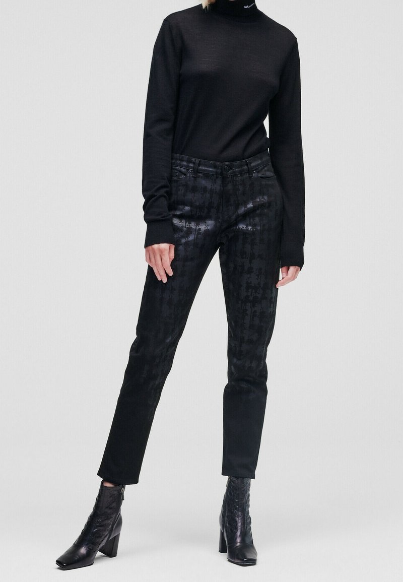 Svart polotröja matched med svarta, mönstrade skinnybyxor. Strukturerad tyg med subtil lyster. Svarta klackstövlar fulländar outfiten.