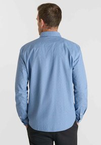 Lichtblauw overhemd met lange mouwen, voorzien van een subtiele textuur, knoopsluiting bij de kraag en knoopjes bij de manchetten. Het heeft een recht design bij de achterste schoudernaad.