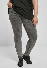 Szürke, skinny farmernadrágok elhalványult textúr�ával, amelyek normál derékrésszel és kontrasztos varrásokkal rendelkeznek. Fekete sportcipőkkel és egy laza fekete felsővel párosítva.