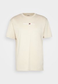 Béžové bavlněné tričko s krátkým rukávem a kulatým výstřihem. Na hrudi se nachází červené, bílé a modré logo "Tommy Jeans".