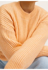 Lichtoranje geribde trui met een ronde halslijn en lange mouwen, die een zachte textuur en een comfortabele pasvorm toont.