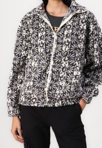 Kurtka z miękkiego materiału na zamek błyskawiczny w czarno-biały kwiatowy wzór, z wysokim kołnierzem i bocznymi kieszeniami, wykonana z teksturowanej tkaniny z elastycznymi mankietami.
