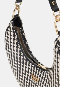 Sac en toile tissé noir et crème, avec une fermeture éclair et des détails en métal doré, présentant un design arrondi. Accents en cuir lisse.