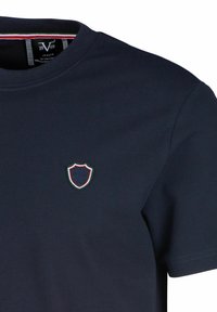 Navyblaues Baumwoll-T-Shirt mit Rundhalsausschnitt, kurzen Ärmeln und einem kleinen gestickten Wappenlogo mit roten und grünen Akzenten.