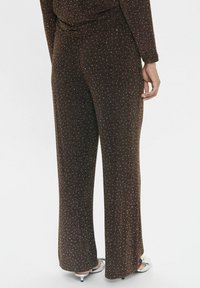 Bruine, glinsterende wijde broek gemaakt van een gestructureerde stof, met kleine, verspreide metallic accenten. Elastische tailleband zichtbaar.