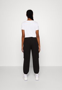 T-shirt en coton blanc à manches courtes, associé à un pantalon cargo noir avec poches latérales et poignets élastiques, porté avec des baskets blanches.