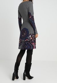 Knielanges Kleid mit einem strukturierten, eng anliegenden schwarzen Oberteil und einem farbenfrohen, gemusterten Rock. Mit langen Ärmeln und schwarzen knöchelhohen Stiefeln.