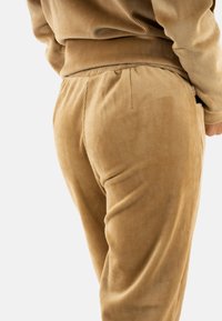 Pantalones de pana en marrón claro, con canalones verticales, una cinturilla elástica y bolsillos laterales. La textura parece suave y acogedora.