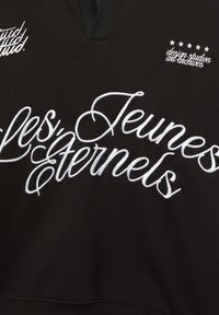 Zwarte sweatshirt met witte geborduurde tekst "les Jeunes Éternels" en een klein logo met sterren aan de linkerbovenkant.