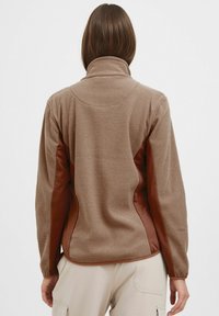 Brown textured jacket with a high collar and smooth brown side panels. Features a pattern throughout and soft fabric for comfort.