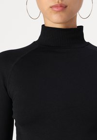 Black turtleneck top made of stretchy fabric with ribbed texture at the collar and shoulder seams, fitted design, and no visible patterns.