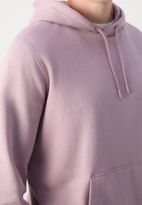 Jasnofioletowa bluza z kapturem wykonana z miękkiego materiału, posiada przednią kieszeń oraz sznurki przy kapturze. Teksturowana powierzchnia o gładkim wykończeniu.